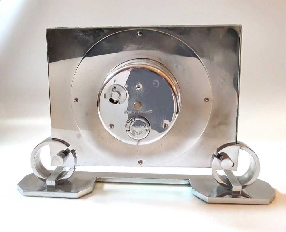 An Art Deco mantel clock featuring a thick rectangular glass body held by chrome scroll mounts on a flat metal base. View XII