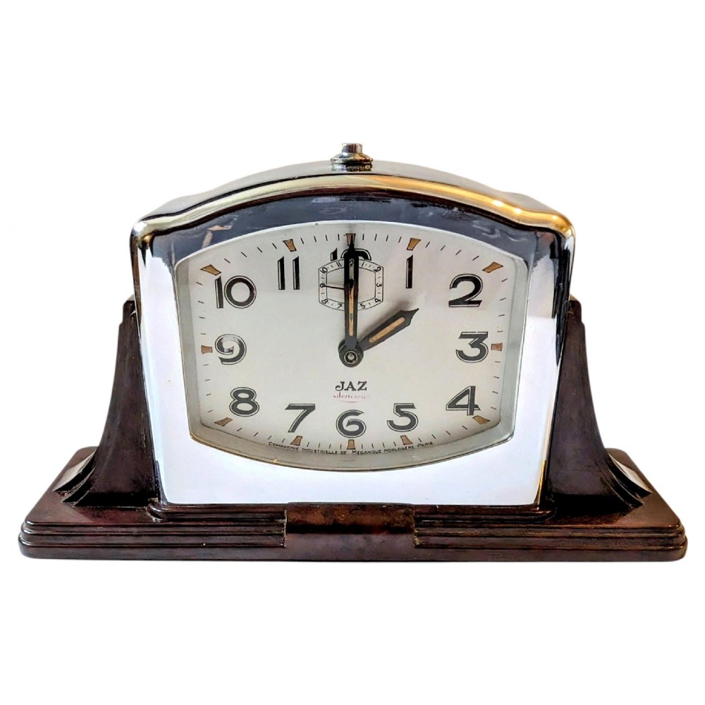 An Art Deco desk clock featuring a dark brown Bakelite stepped base, a polished chrome frame, and a cream dial with geometric Arabic numerals. View IV