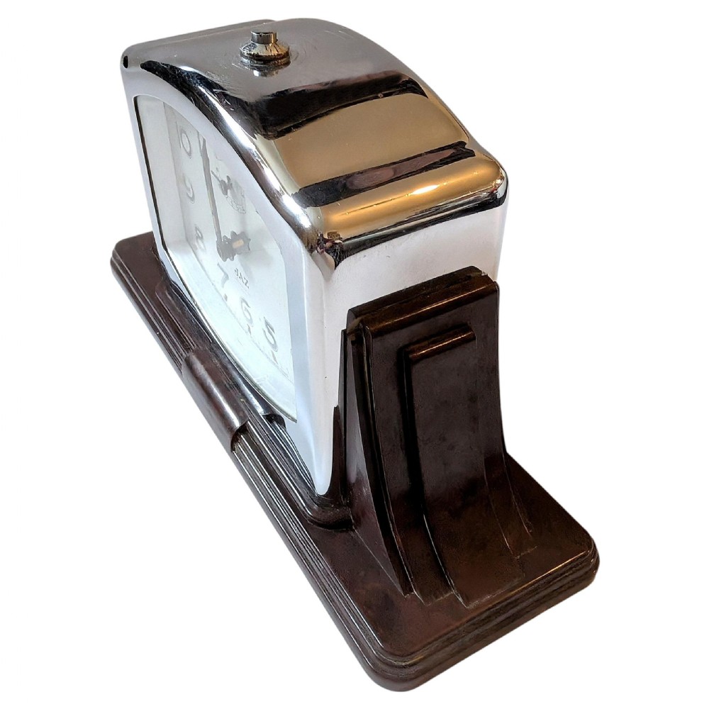 An Art Deco desk clock featuring a dark brown Bakelite stepped base, a polished chrome frame, and a cream dial with geometric Arabic numerals. View V