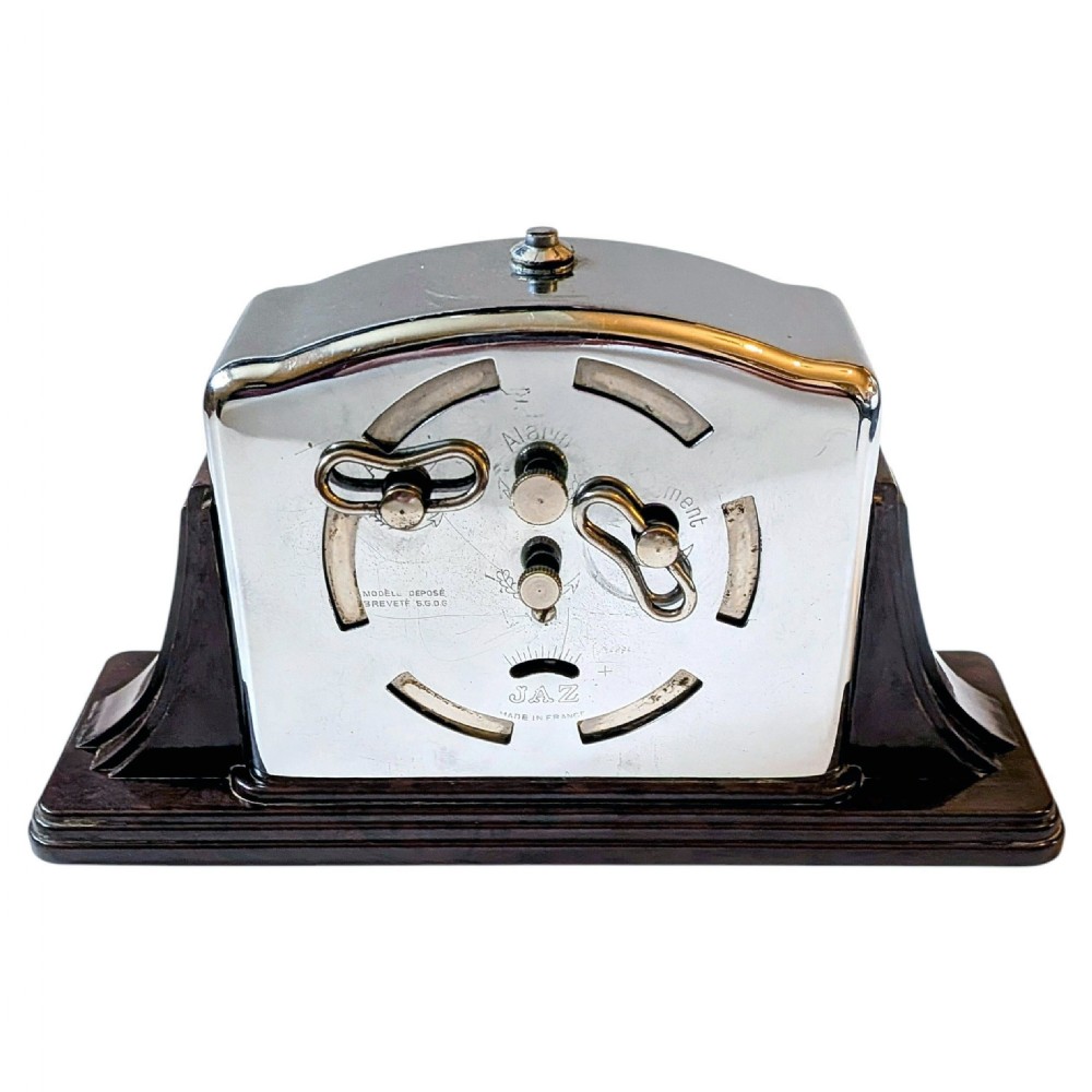 An Art Deco desk clock featuring a dark brown Bakelite stepped base, a polished chrome frame, and a cream dial with geometric Arabic numerals. View VI