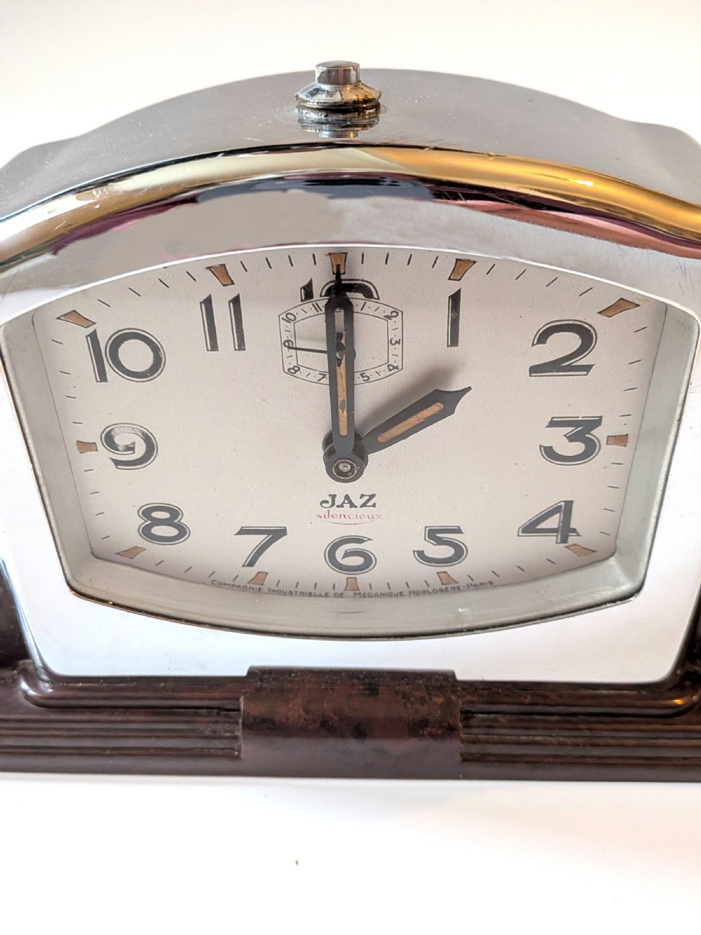 An Art Deco desk clock featuring a dark brown Bakelite stepped base, a polished chrome frame, and a cream dial with geometric Arabic numerals. View VIII
