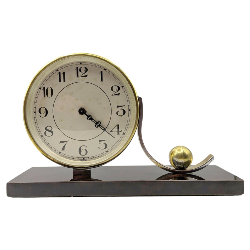 An Art Deco desk clock featuring a circular brass dial and stylised wave element resting on a rectangular dark brown Bakelite base.