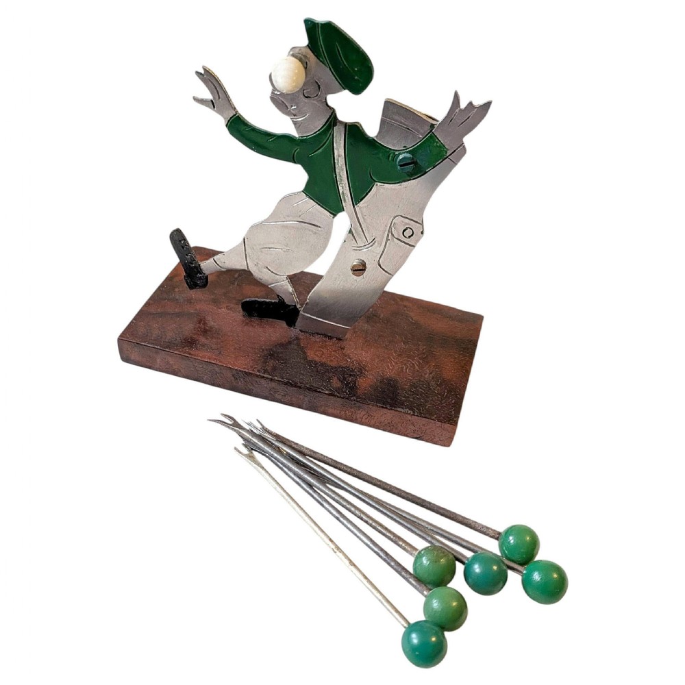 An Art Deco metal cocktail pick set shaped as a stylised golfer figure wearing a green cap and top, mounted on a rectangular brown base holding green-topped picks. View II