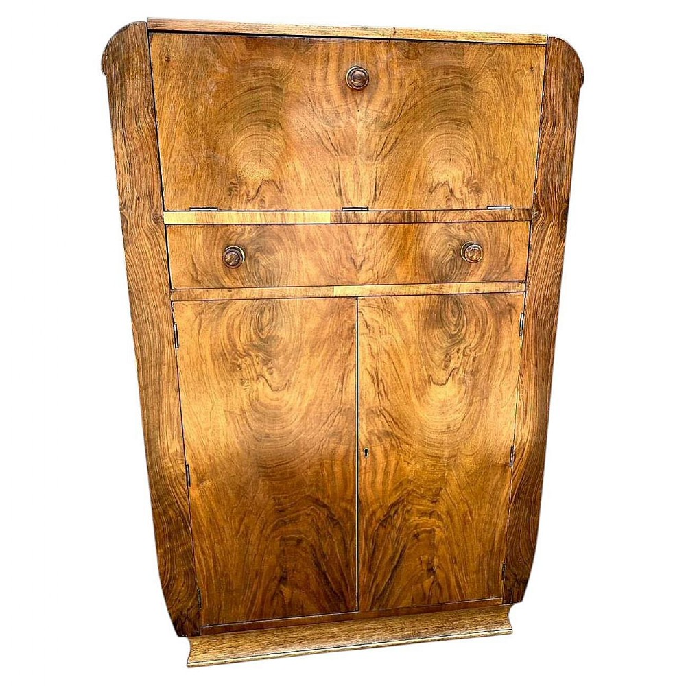 An Art Deco figured walnut cocktail cabinet featuring a fall-front upper flap, a central drawer, and two lower cupboard doors.