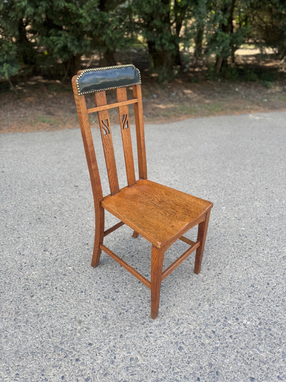 An Arts and Crafts solid oak side chair featuring a vertical pierced slat back and a brass-studded leather padded top crest rail.