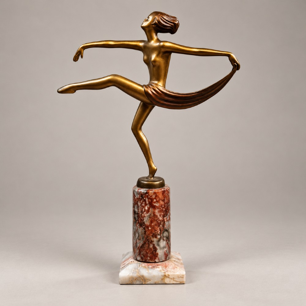 An Art Deco bronzed spelter figurine of a female scarf dancer mounted on a cylindrical variegated marble pedestal.