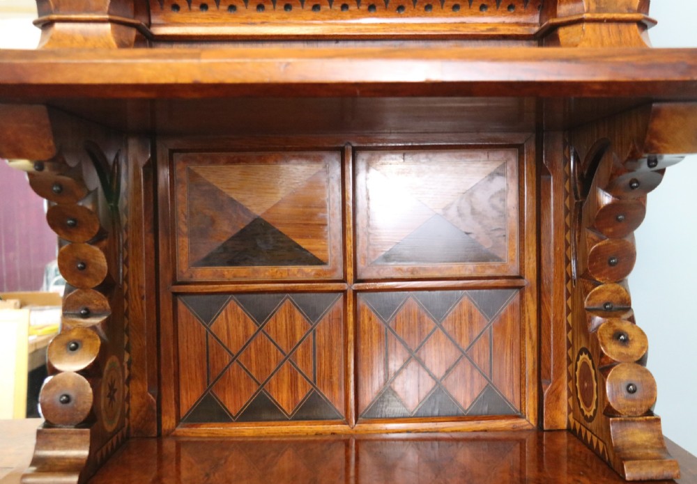 A Victorian Gothic Revival sideboard crafted from pollard oak featuring intricate geometric wood inlays, turned black columns, twin pedestal cupboards, and a tiered upper superstructure. View XVIII