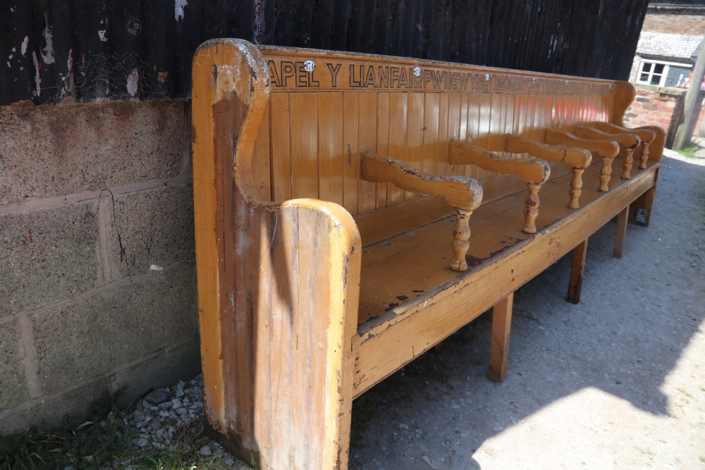A long Victorian painted pine chapel bench featuring a vertical panelled back, turned arm dividers, and Welsh script along the top rail. View II