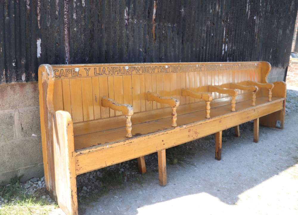 A long Victorian painted pine chapel bench featuring a vertical panelled back, turned arm dividers, and Welsh script along the top rail. View V