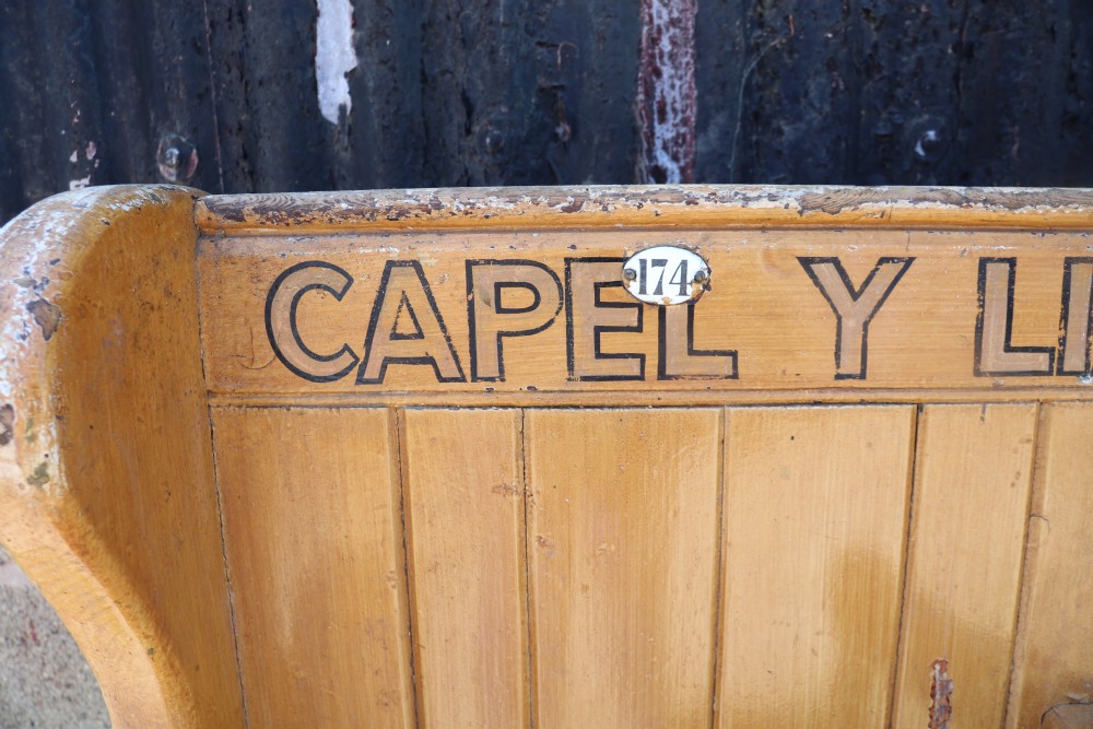 A long Victorian painted pine chapel bench featuring a vertical panelled back, turned arm dividers, and Welsh script along the top rail. View XIV