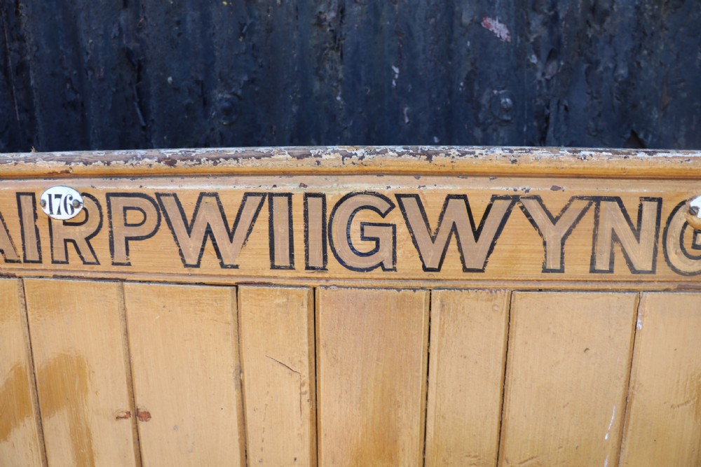 A long Victorian painted pine chapel bench featuring a vertical panelled back, turned arm dividers, and Welsh script along the top rail. View XV