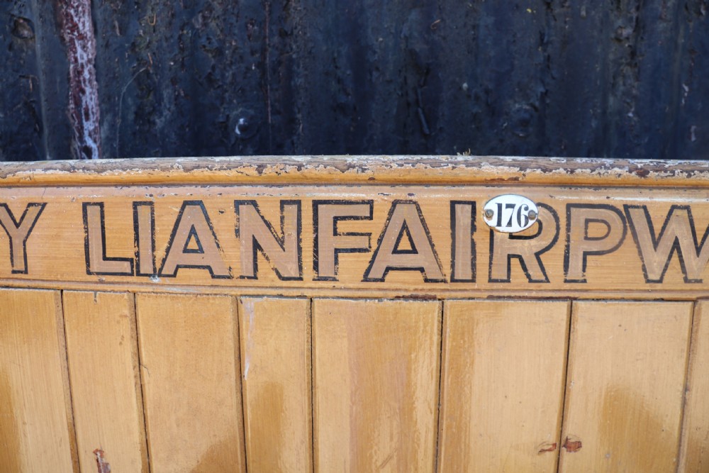 A long Victorian painted pine chapel bench featuring a vertical panelled back, turned arm dividers, and Welsh script along the top rail. View XVI
