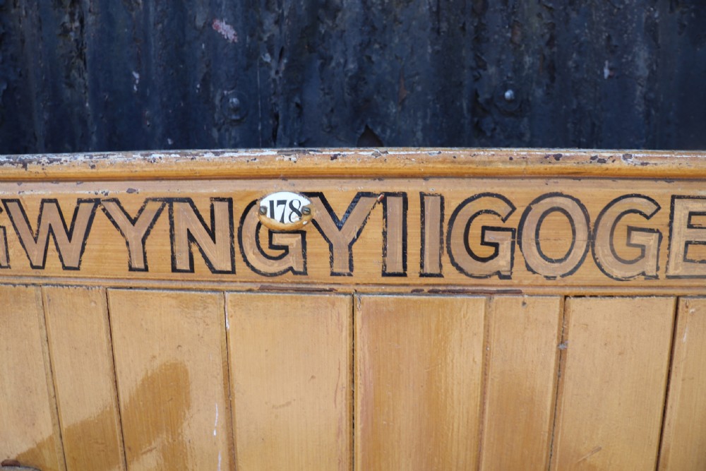 A long Victorian painted pine chapel bench featuring a vertical panelled back, turned arm dividers, and Welsh script along the top rail. View XVII