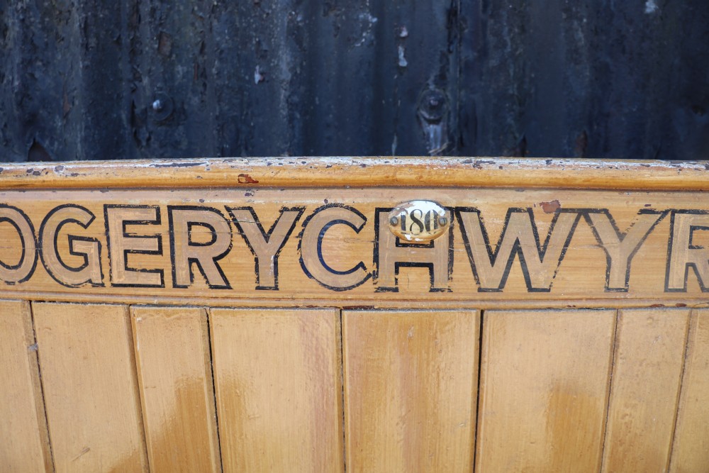 A long Victorian painted pine chapel bench featuring a vertical panelled back, turned arm dividers, and Welsh script along the top rail. View XVIII