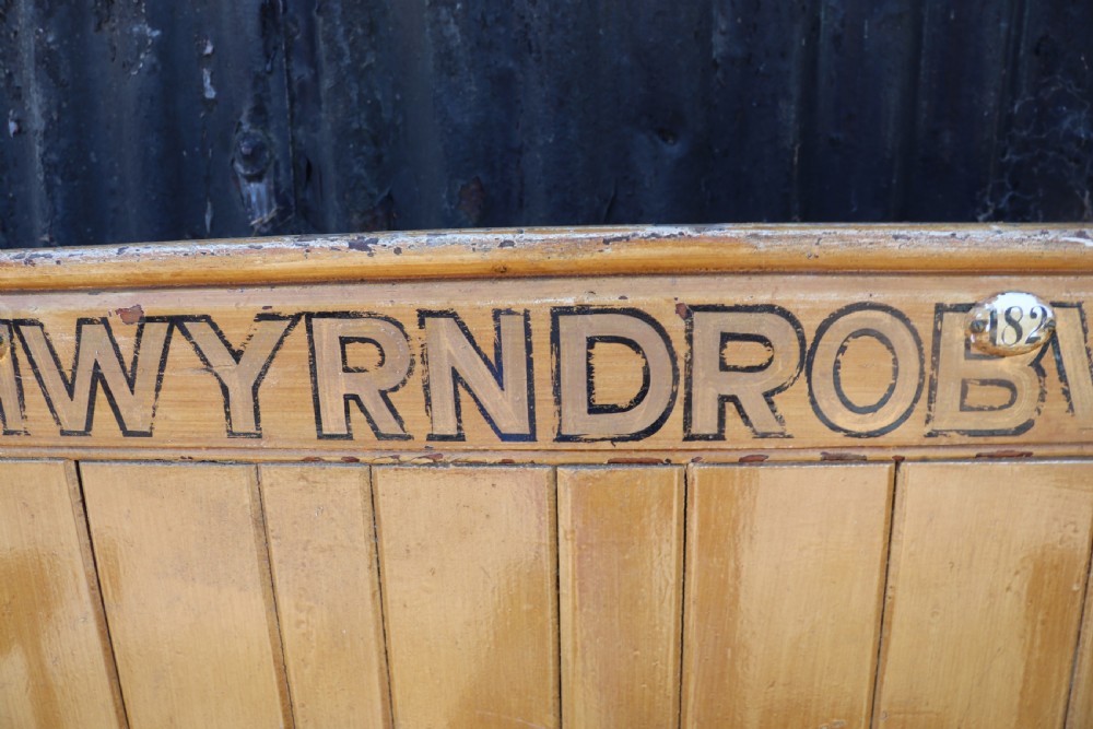 A long Victorian painted pine chapel bench featuring a vertical panelled back, turned arm dividers, and Welsh script along the top rail. View XIX