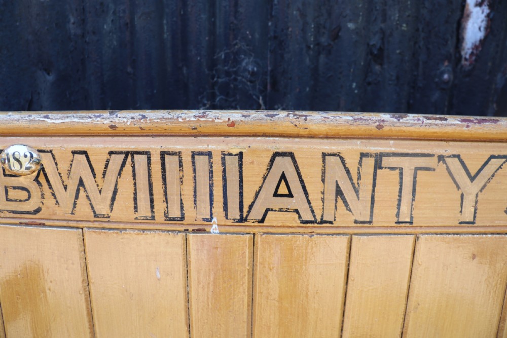 A long Victorian painted pine chapel bench featuring a vertical panelled back, turned arm dividers, and Welsh script along the top rail. View XX