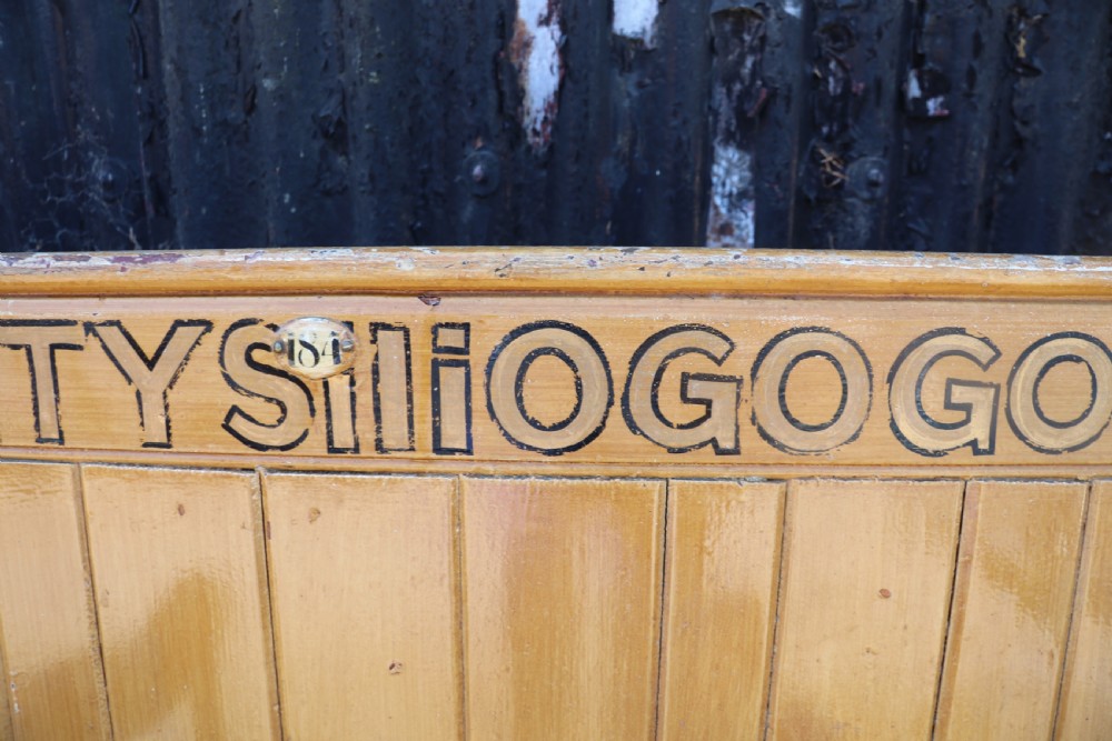 A long Victorian painted pine chapel bench featuring a vertical panelled back, turned arm dividers, and Welsh script along the top rail. View XXI