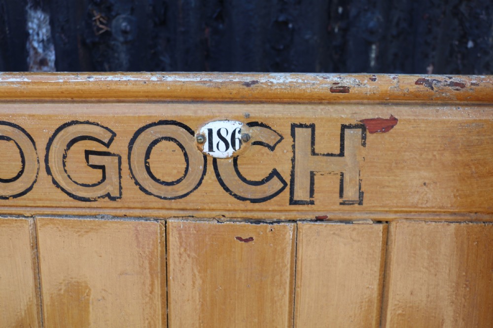 A long Victorian painted pine chapel bench featuring a vertical panelled back, turned arm dividers, and Welsh script along the top rail. View XXII