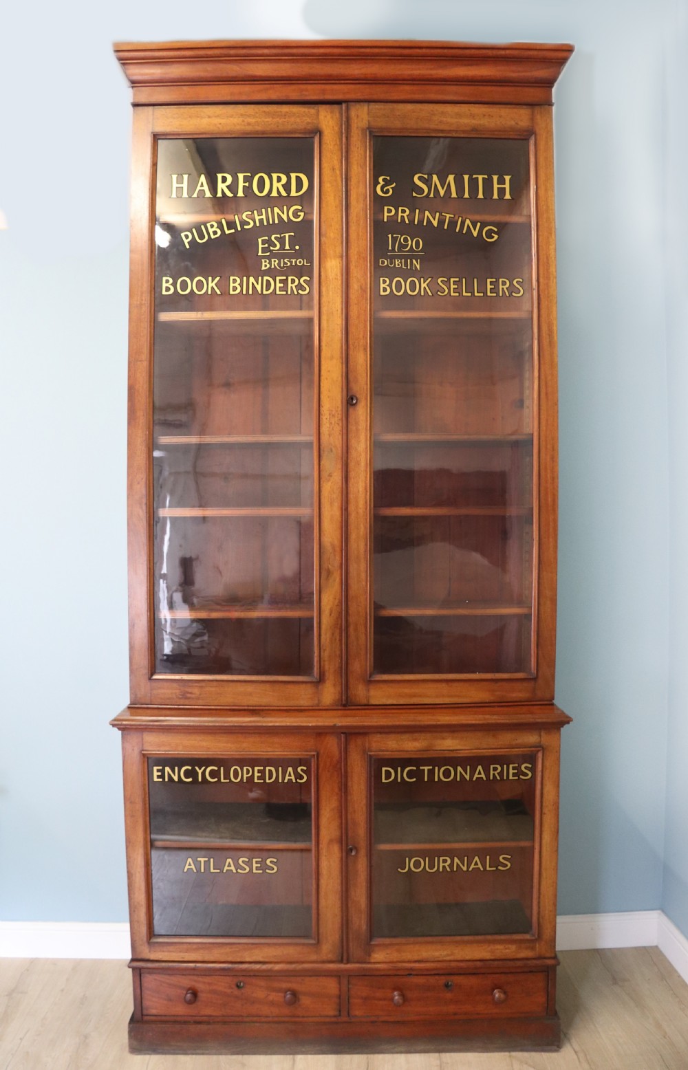 A tall Victorian mahogany two-section bookcase cabinet featuring double glazed doors adorned with gilt lettering above lower glazed doors and drawers. View II