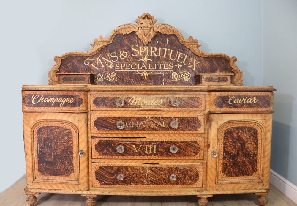 A nineteenth-century French Chateau style walnut sideboard featuring hand-painted French typography, decorative faux-marbling, a carved crest, and glass drawer knobs.