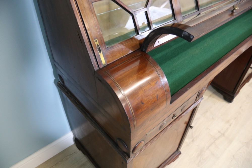 An early nineteenth-century mahogany twin pedestal display cabinet featuring glazed upper doors with geometric glazing bars, a central curved glass display section, and inlaid pedestal cupboards below. View VII