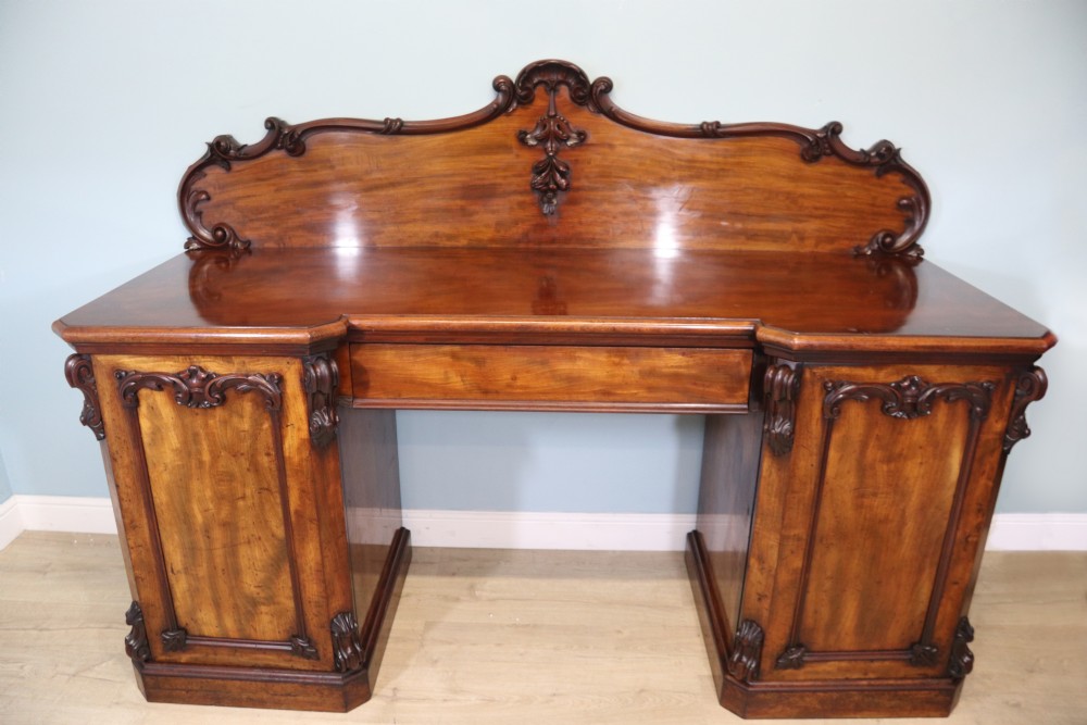 A Victorian mahogany twin pedestal sideboard featuring a central frieze drawer, carved splashback, and flame mahogany cupboard doors on plinth bases. View II