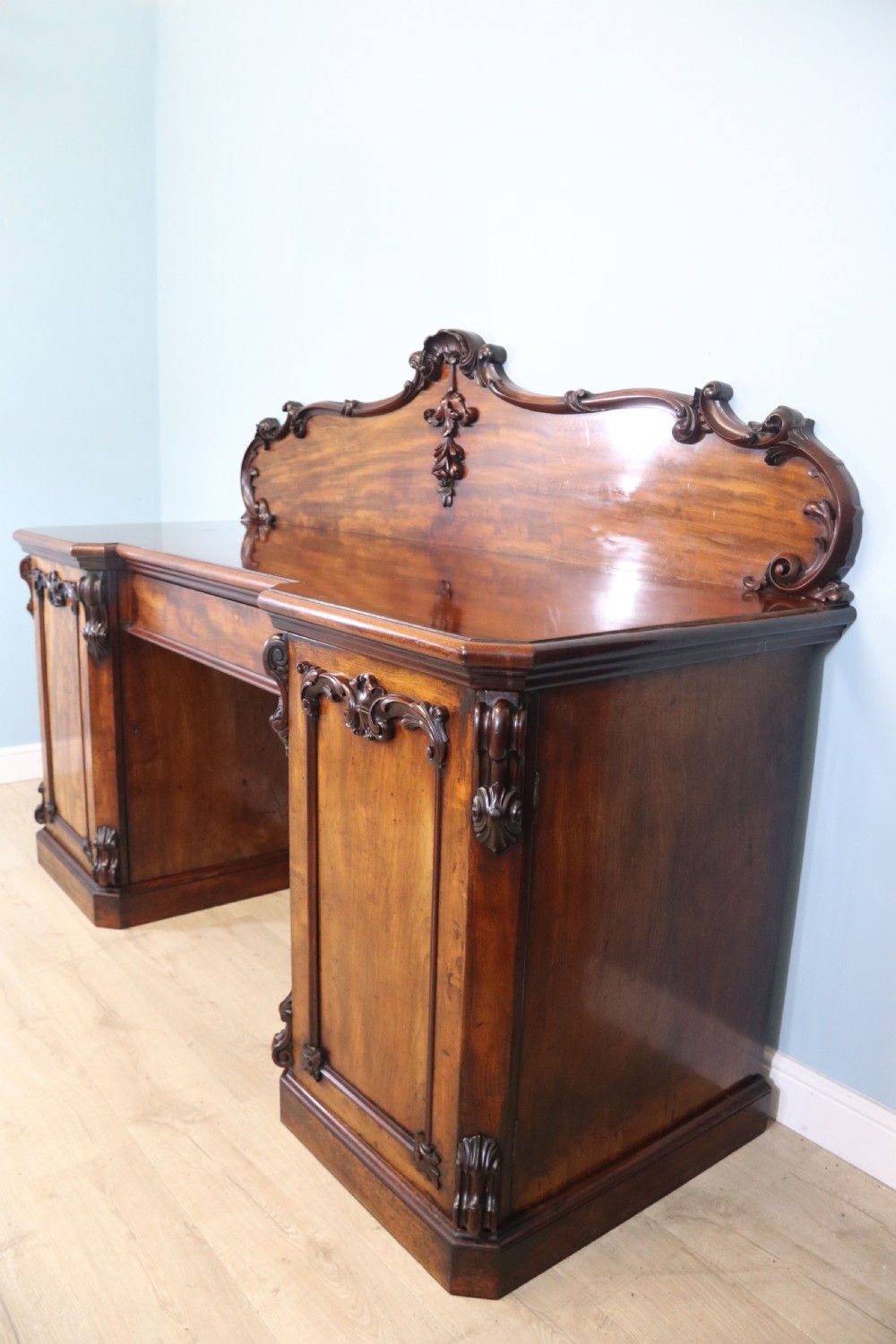 A Victorian mahogany twin pedestal sideboard featuring a central frieze drawer, carved splashback, and flame mahogany cupboard doors on plinth bases. View III