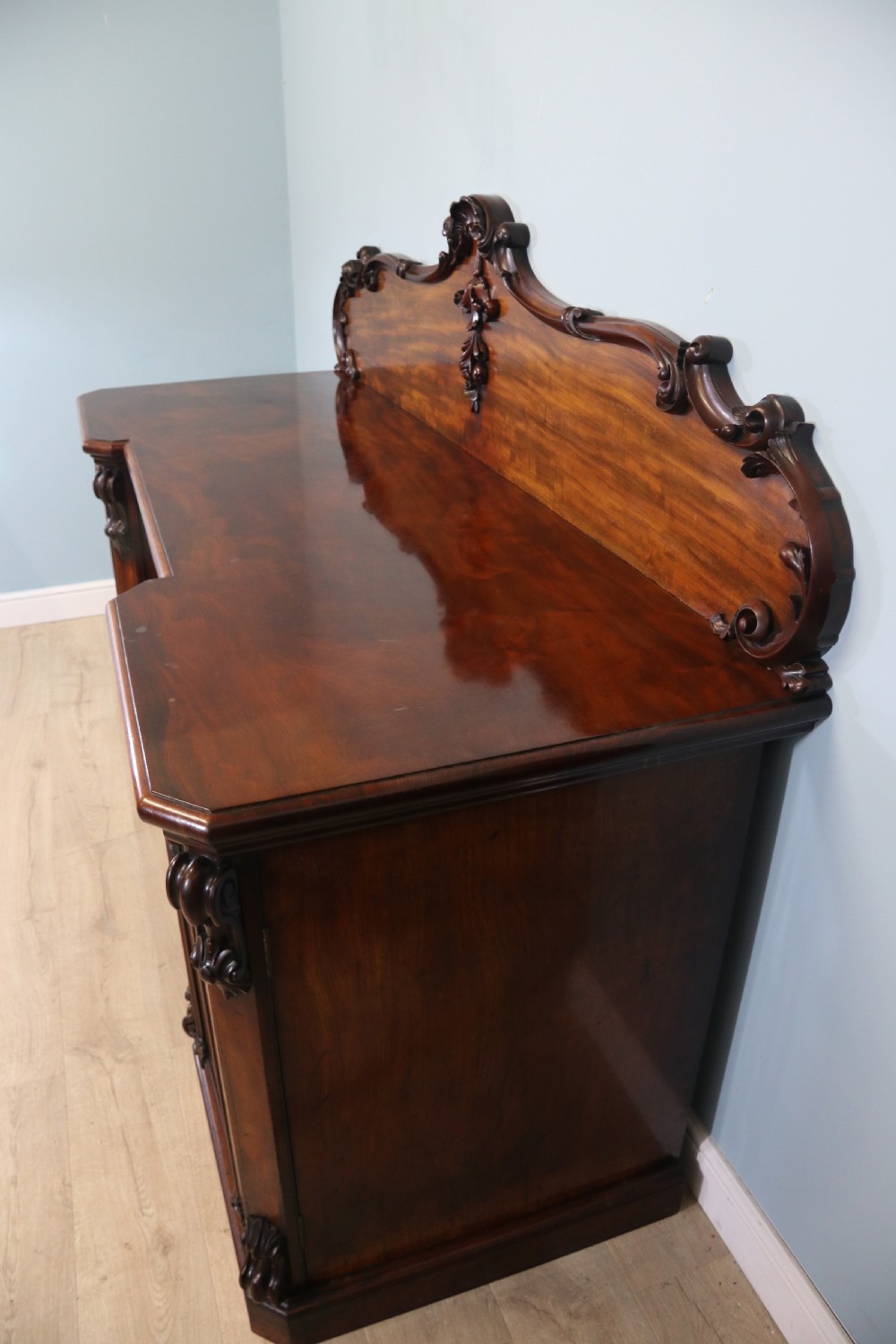 A Victorian mahogany twin pedestal sideboard featuring a central frieze drawer, carved splashback, and flame mahogany cupboard doors on plinth bases. View IV