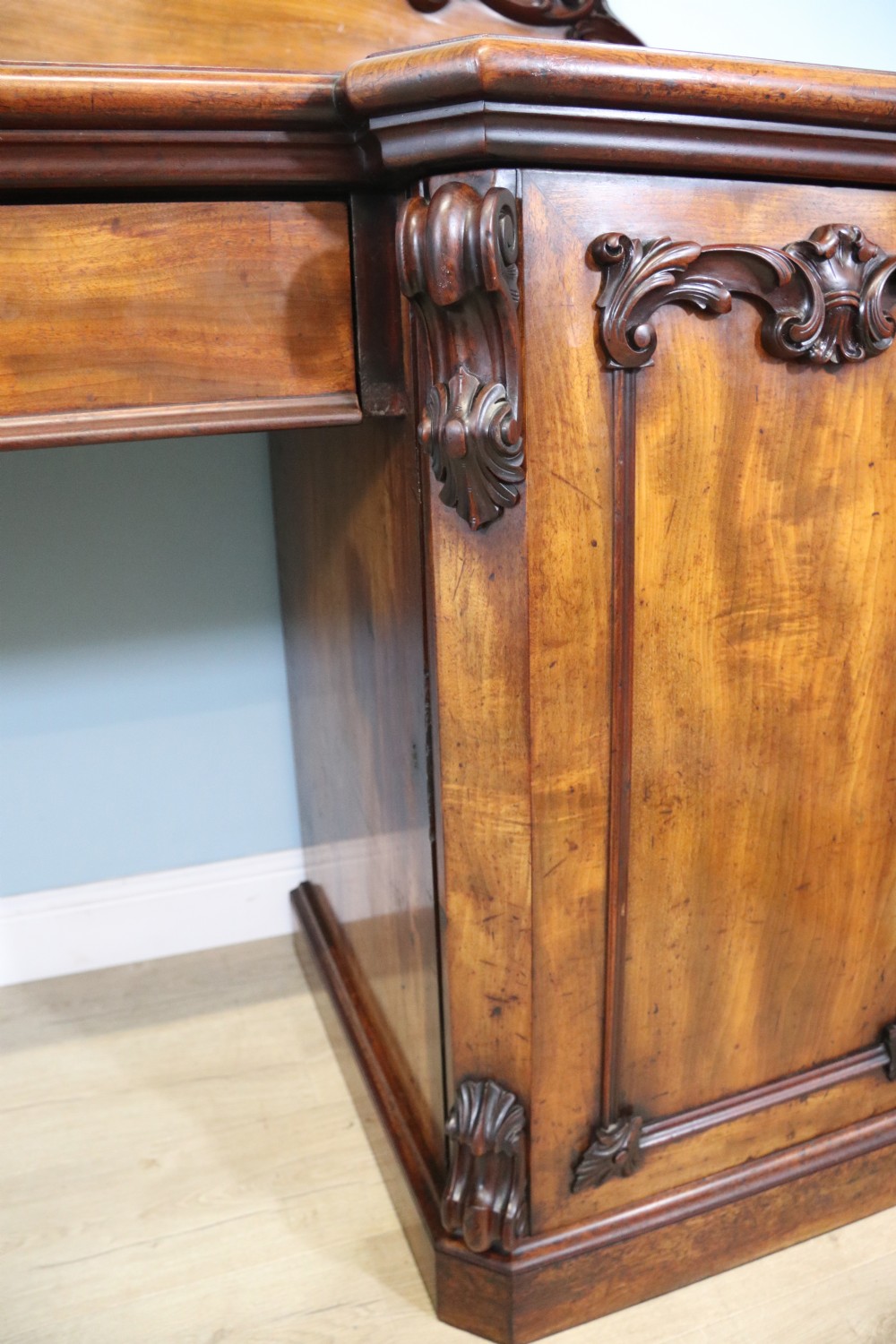 A Victorian mahogany twin pedestal sideboard featuring a central frieze drawer, carved splashback, and flame mahogany cupboard doors on plinth bases. View VI