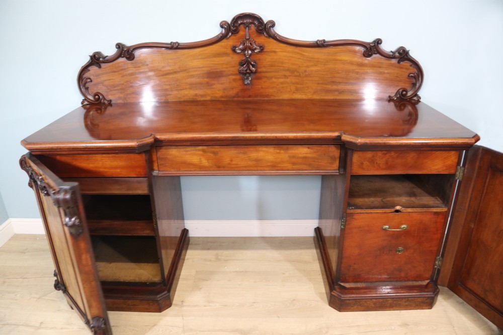 A Victorian mahogany twin pedestal sideboard featuring a central frieze drawer, carved splashback, and flame mahogany cupboard doors on plinth bases. View VII