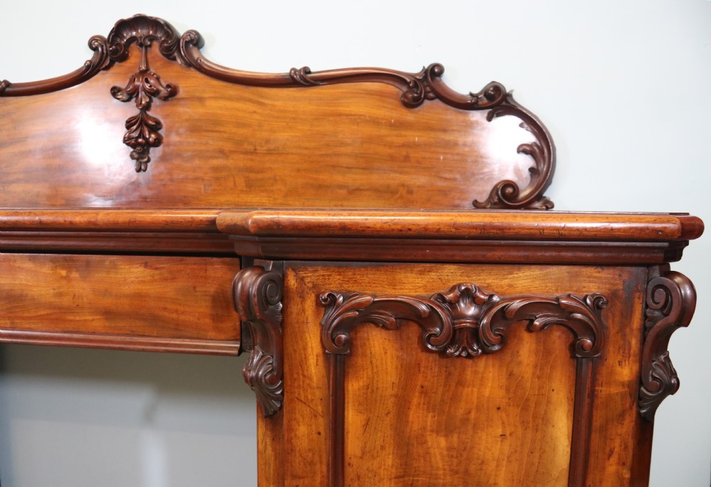 A Victorian mahogany twin pedestal sideboard featuring a central frieze drawer, carved splashback, and flame mahogany cupboard doors on plinth bases. View VIII