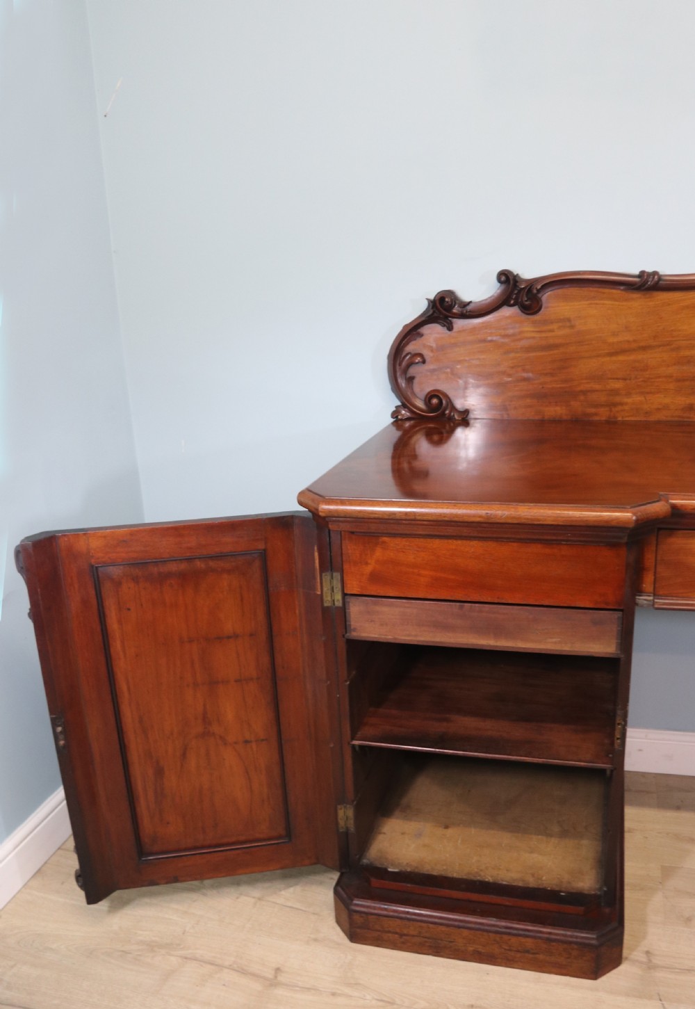 A Victorian mahogany twin pedestal sideboard featuring a central frieze drawer, carved splashback, and flame mahogany cupboard doors on plinth bases. View IX
