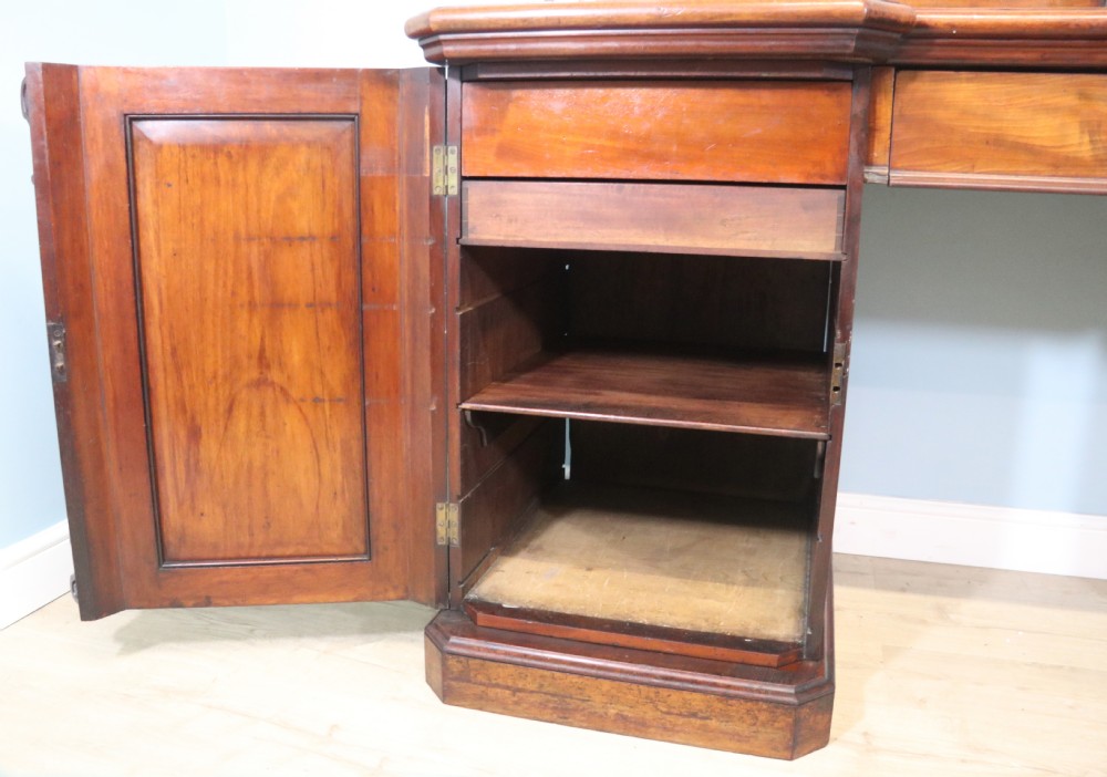 A Victorian mahogany twin pedestal sideboard featuring a central frieze drawer, carved splashback, and flame mahogany cupboard doors on plinth bases. View X