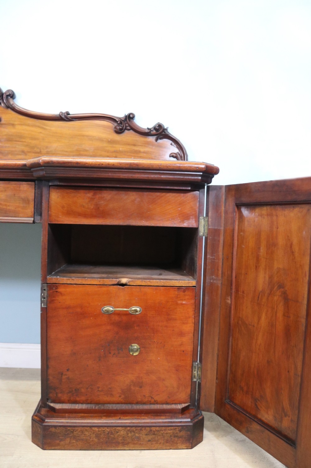 A Victorian mahogany twin pedestal sideboard featuring a central frieze drawer, carved splashback, and flame mahogany cupboard doors on plinth bases. View XI