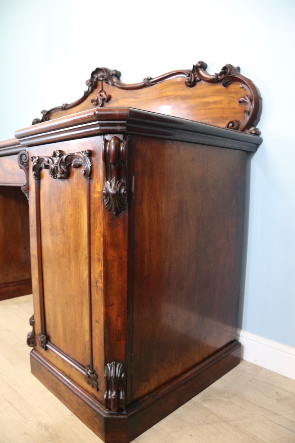 A Victorian mahogany twin pedestal sideboard featuring a central frieze drawer, carved splashback, and flame mahogany cupboard doors on plinth bases. View XV