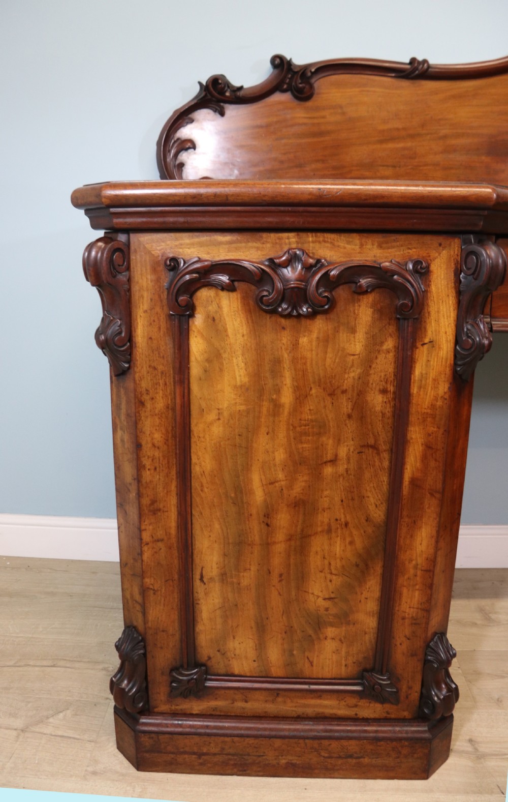 A Victorian mahogany twin pedestal sideboard featuring a central frieze drawer, carved splashback, and flame mahogany cupboard doors on plinth bases. View XVI