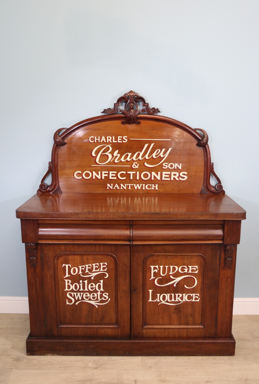 A Victorian mahogany chiffonier featuring hand-painted cream and red commercial typography across the upper cresting back and lower cupboard doors.