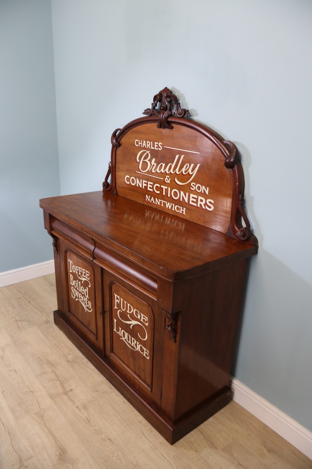 A Victorian mahogany chiffonier featuring hand-painted cream and red commercial typography across the upper cresting back and lower cupboard doors. View II