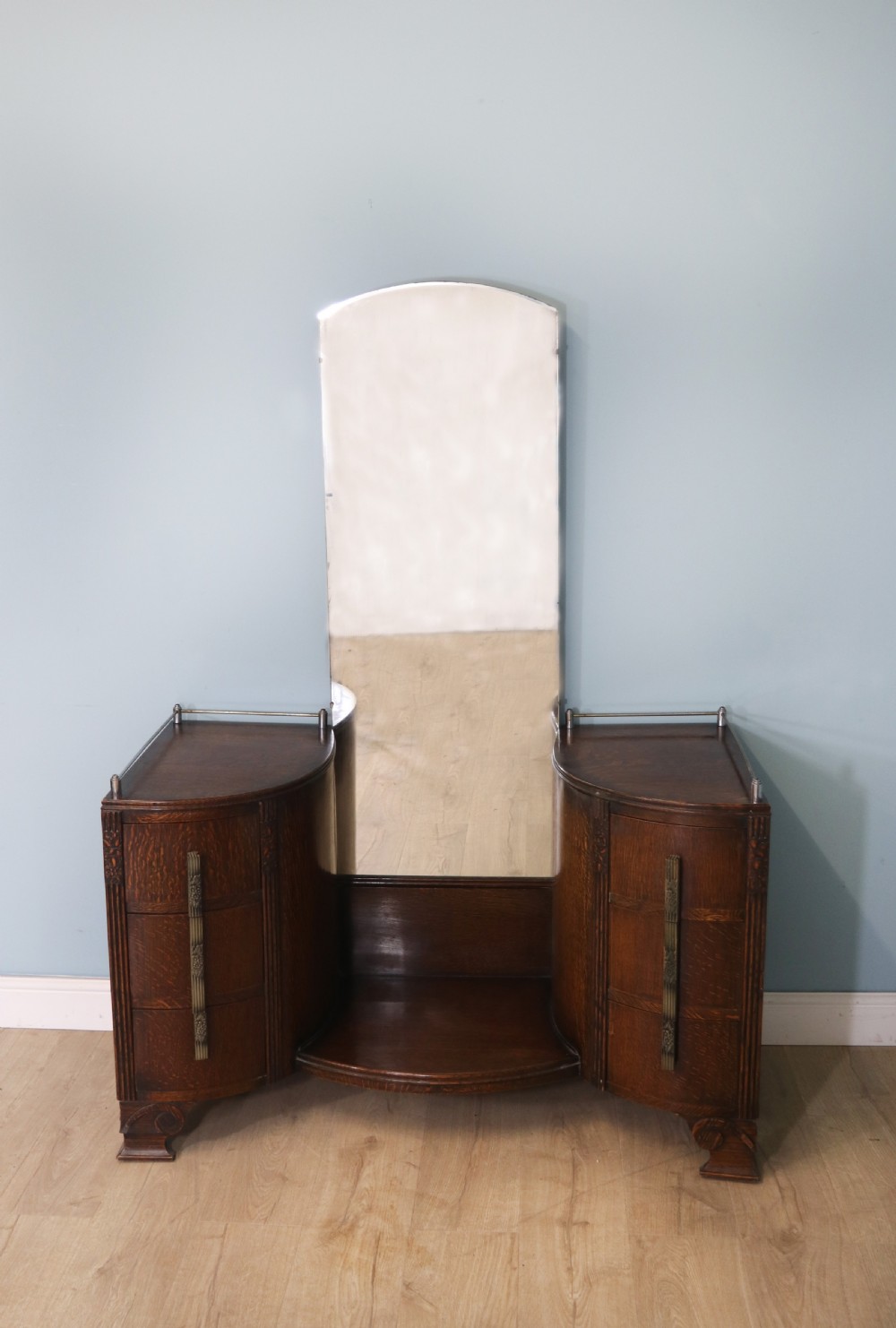 An Art Deco dark oak twin pedestal dressing chest featuring a central full-length arched mirror flanked by two curved three-drawer pedestals with metal gallery rails.