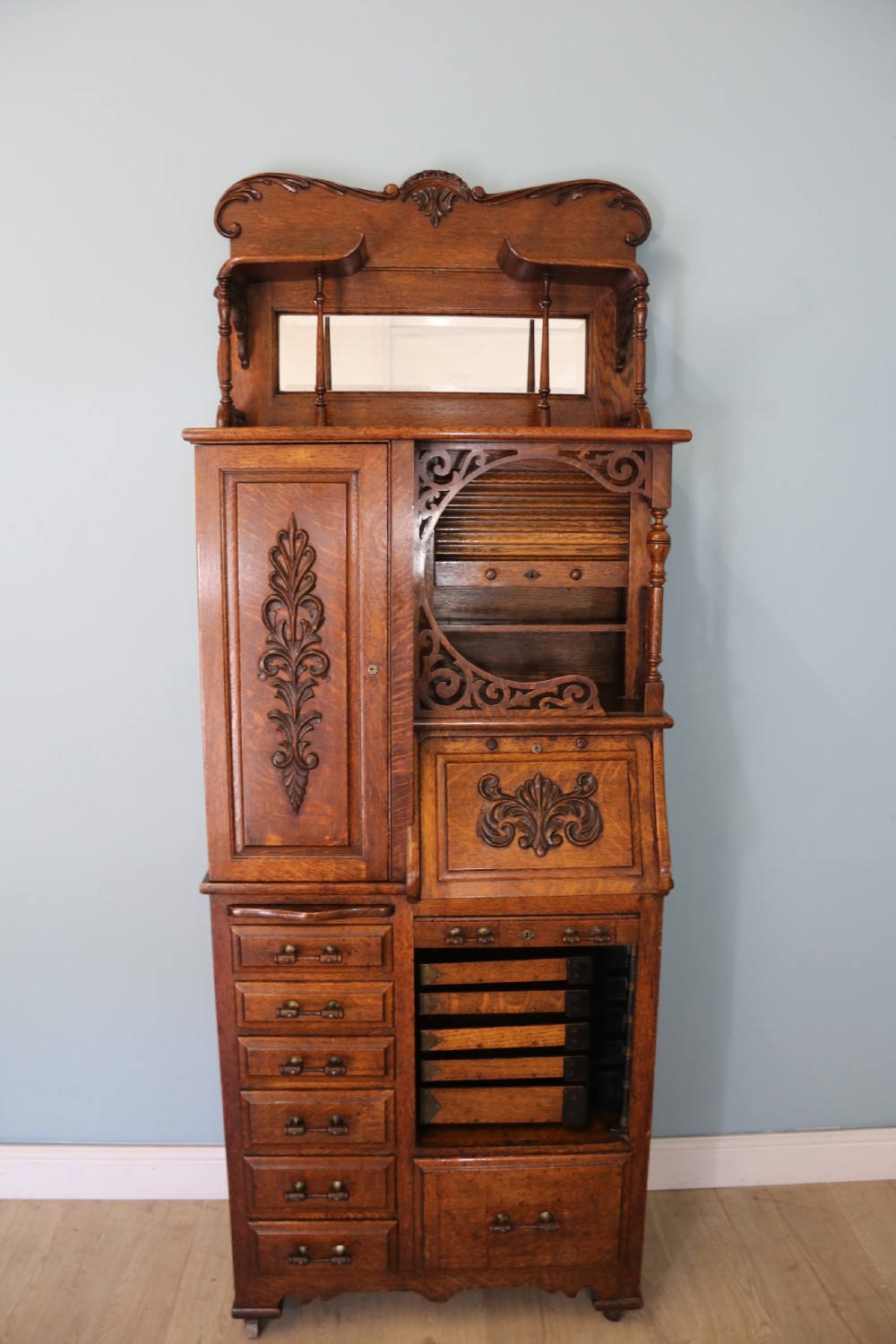 A late nineteenth-century oak combination dentist cabinet featuring a mirrored gallery top, carved foliate door, tambour section, and multiple small drawers. View III