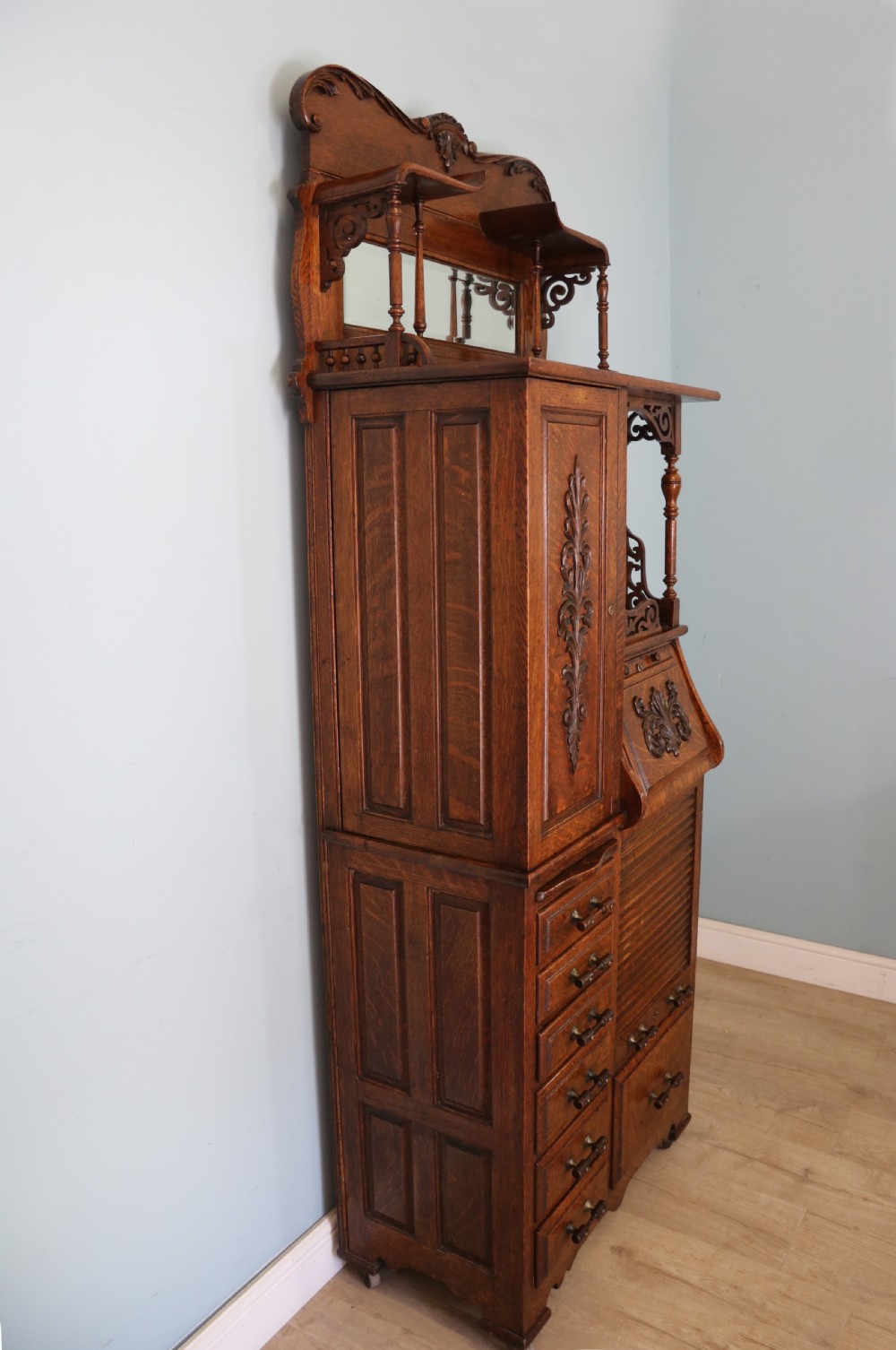 A late nineteenth-century oak combination dentist cabinet featuring a mirrored gallery top, carved foliate door, tambour section, and multiple small drawers. View VII