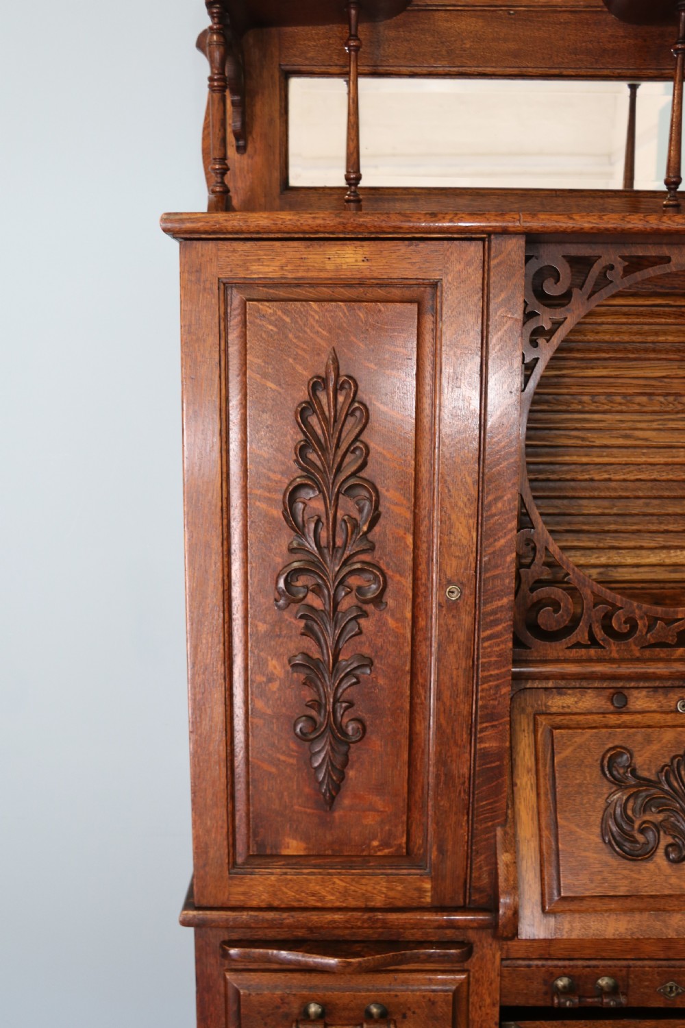 A late nineteenth-century oak combination dentist cabinet featuring a mirrored gallery top, carved foliate door, tambour section, and multiple small drawers. View XVII