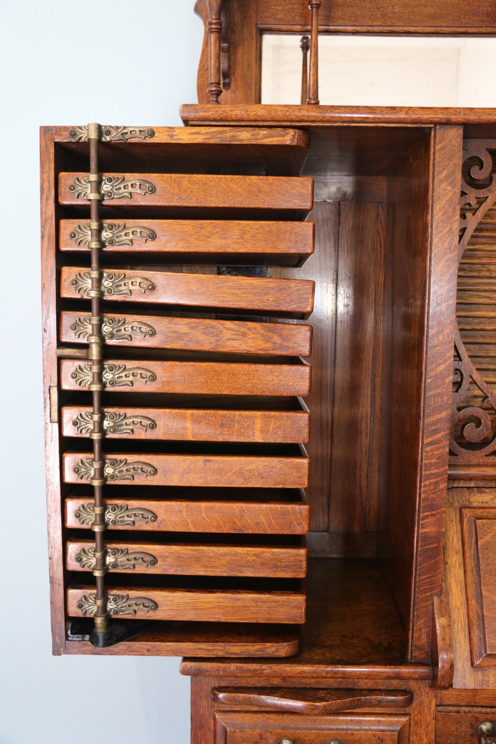 A late nineteenth-century oak combination dentist cabinet featuring a mirrored gallery top, carved foliate door, tambour section, and multiple small drawers. View XIX