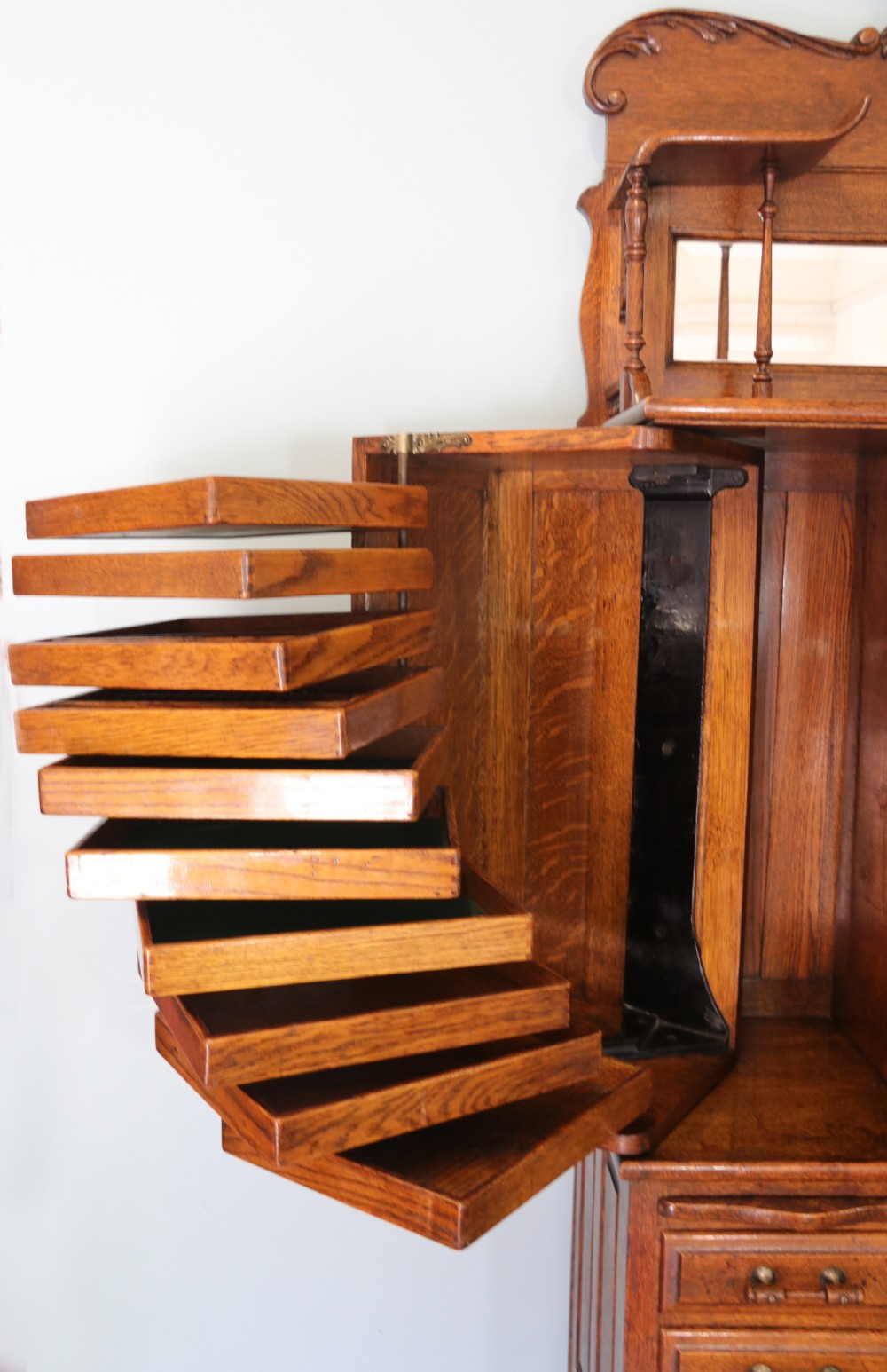 A late nineteenth-century oak combination dentist cabinet featuring a mirrored gallery top, carved foliate door, tambour section, and multiple small drawers. View XXII
