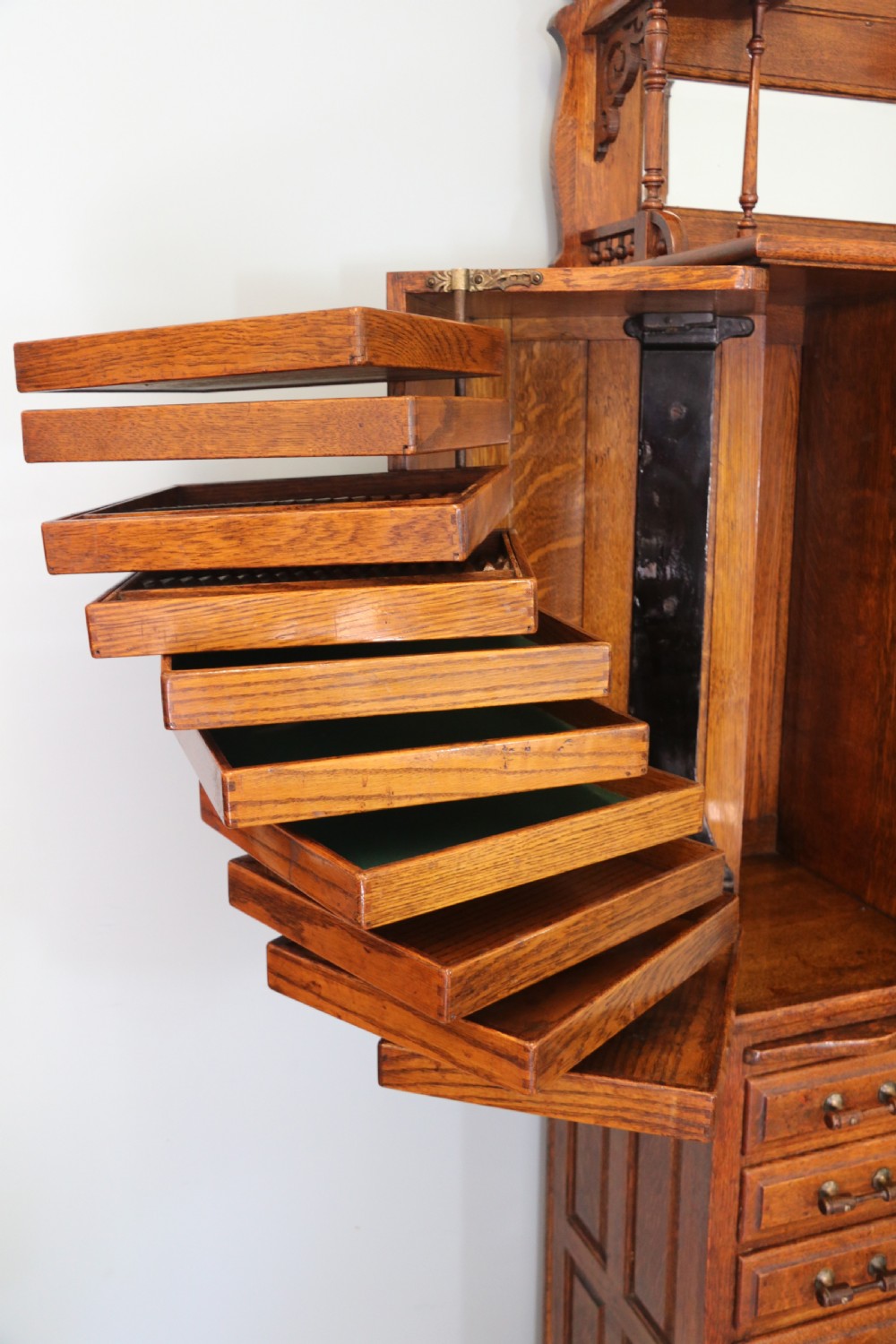 A late nineteenth-century oak combination dentist cabinet featuring a mirrored gallery top, carved foliate door, tambour section, and multiple small drawers. View XXIII