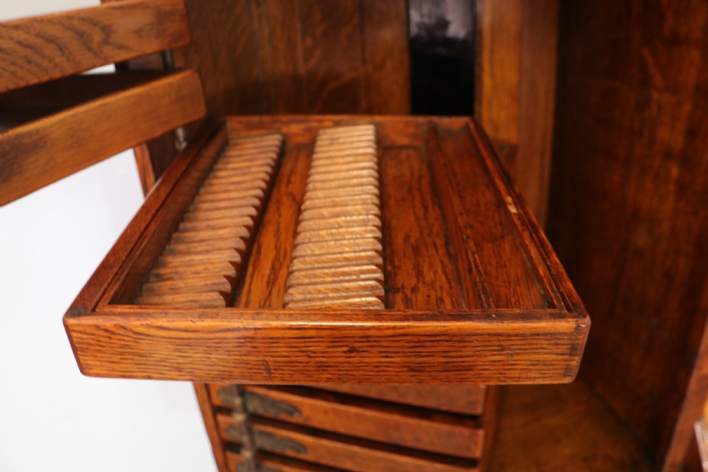 A late nineteenth-century oak combination dentist cabinet featuring a mirrored gallery top, carved foliate door, tambour section, and multiple small drawers. View XXIV