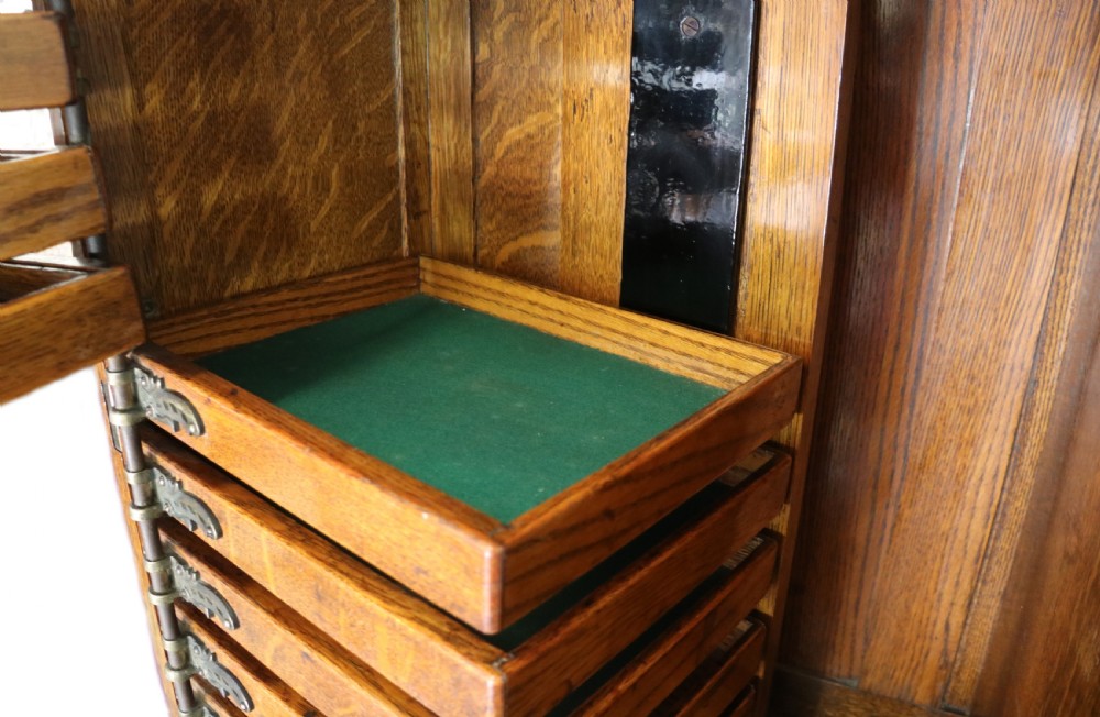 A late nineteenth-century oak combination dentist cabinet featuring a mirrored gallery top, carved foliate door, tambour section, and multiple small drawers. View XXV