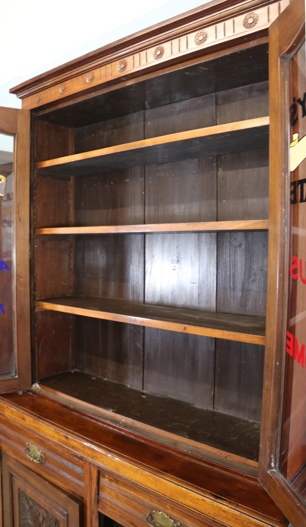 A two-tier dark walnut display cabinet featuring glazed upper doors decorated with vintage Cadburys advertising lettering above lower carved wooden cupboard doors. View III