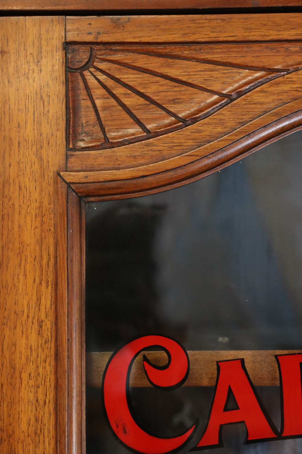 A two-tier dark walnut display cabinet featuring glazed upper doors decorated with vintage Cadburys advertising lettering above lower carved wooden cupboard doors. View VIII
