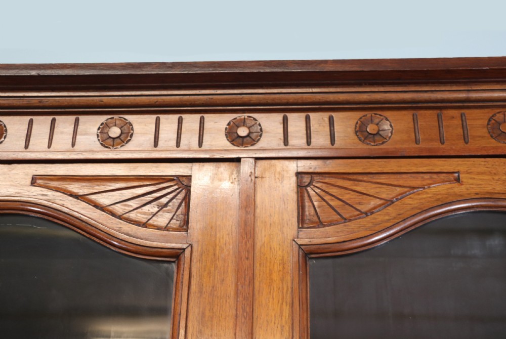 A two-tier dark walnut display cabinet featuring glazed upper doors decorated with vintage Cadburys advertising lettering above lower carved wooden cupboard doors. View IX